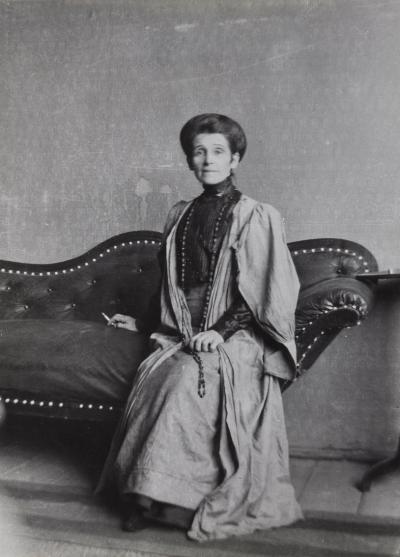 Zdj. nr 49: Olga Boznańska, ok. 1913 - Olga Boznańska w pracowni w domu przy ul. Wolskiej 21 w Krakowie, siedząca na kanapie z papierosem w dłoni, ok. 1913, fotografia, 16,9 x 12,2 cm